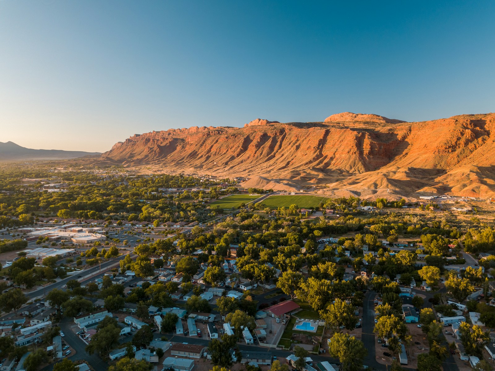 Aerial view of Moab homes and trees beneath red-rock cliffs