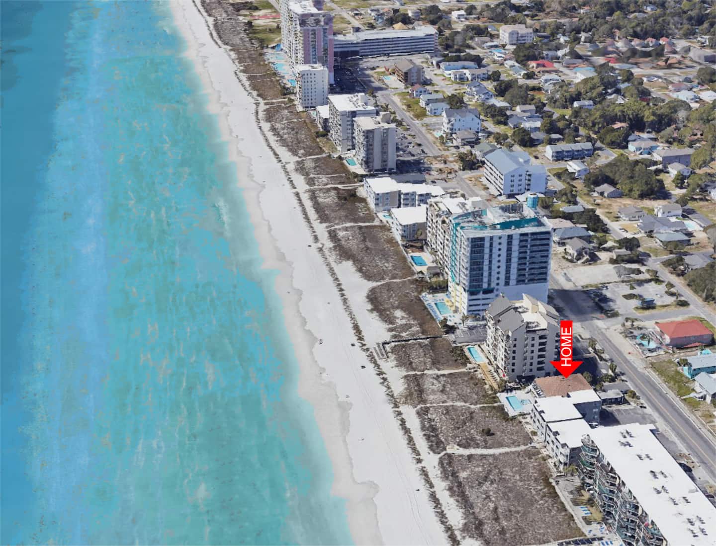 Oblique aerial view of a sandy coastline, ocean, and rows of beachfront buildings.