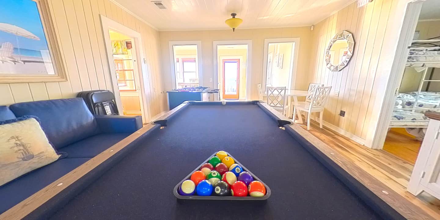 Pool table between blue sofas in a bright room with windows.