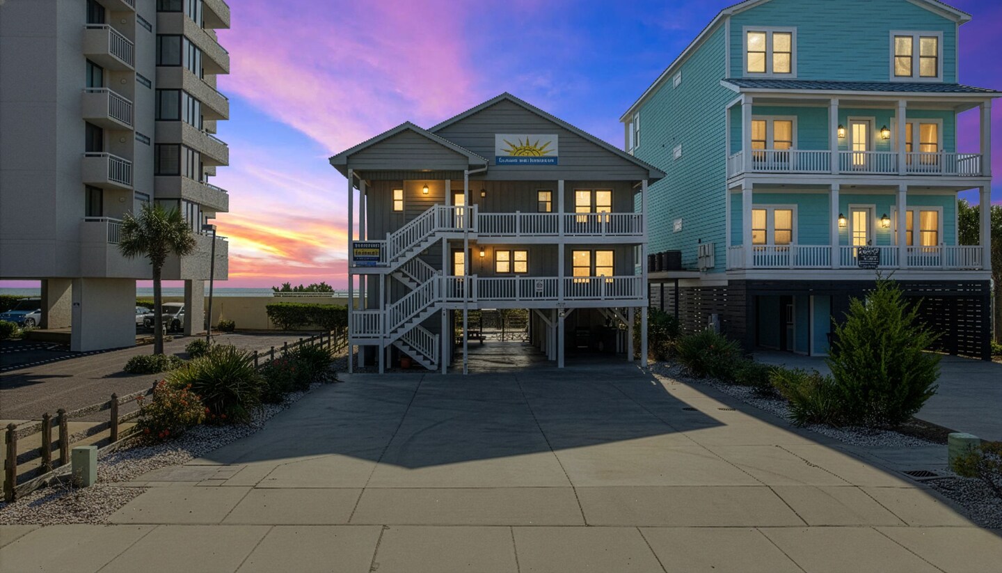 Two neighboring coastal houses and a paved driveway photographed at dusk.