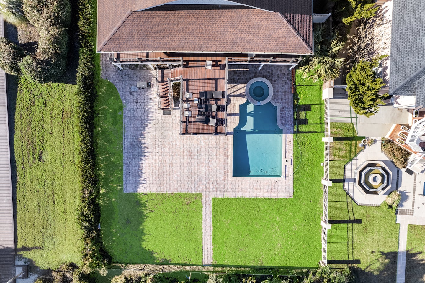 Overhead view of a beachfront house, fenced lawn, swimming pool, and outdoor seating.