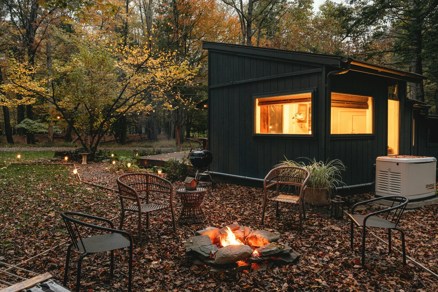 Small black cabin in the woods beside a glowing fire pit