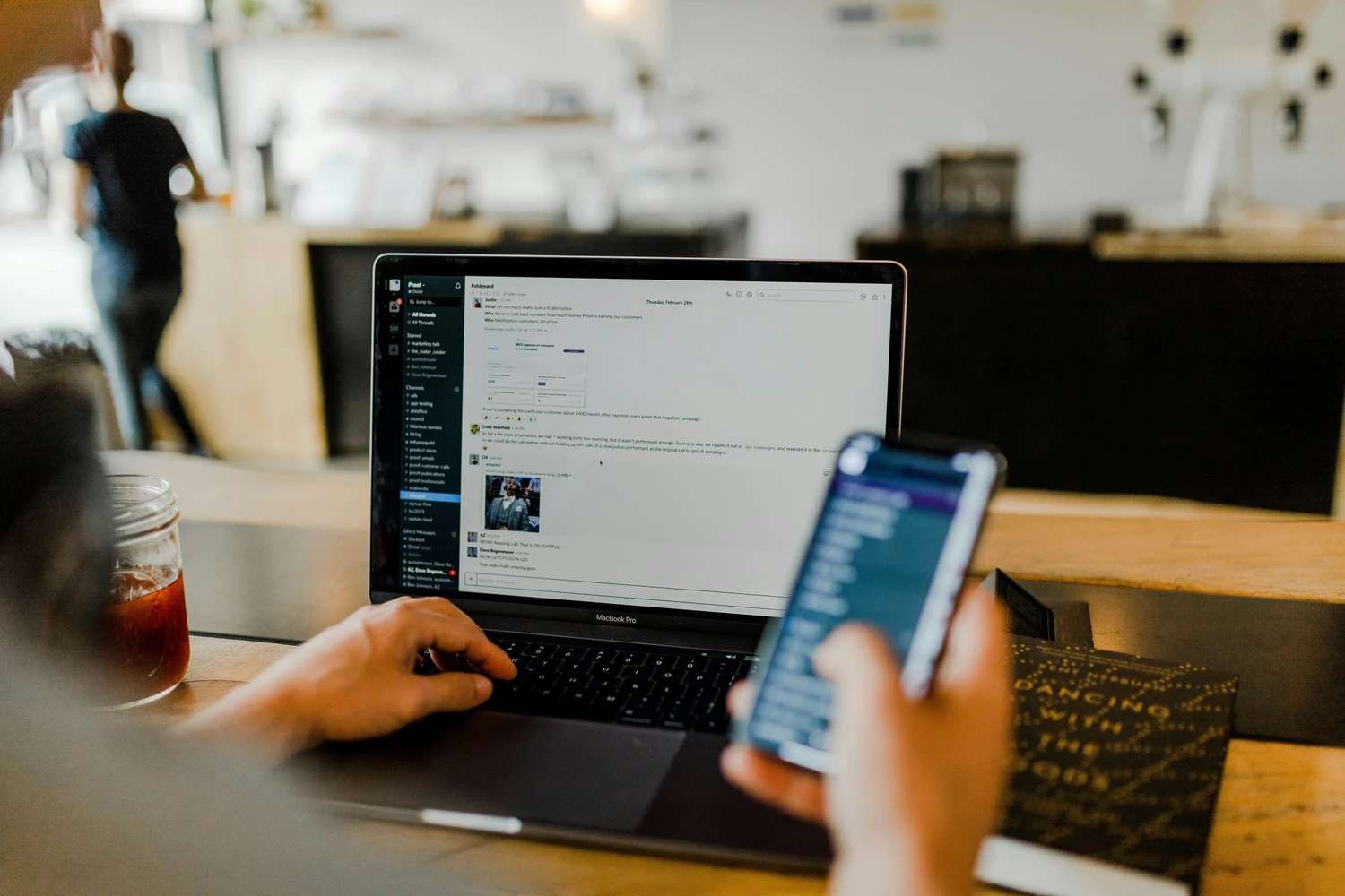 Person using a smartphone beside an open laptop in a cafe