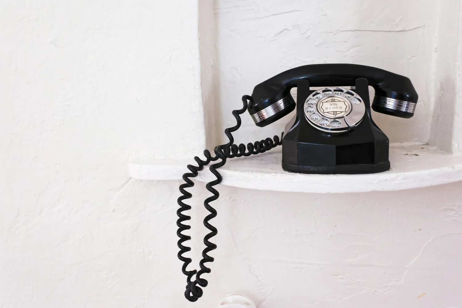 Black rotary telephone on a white shelf