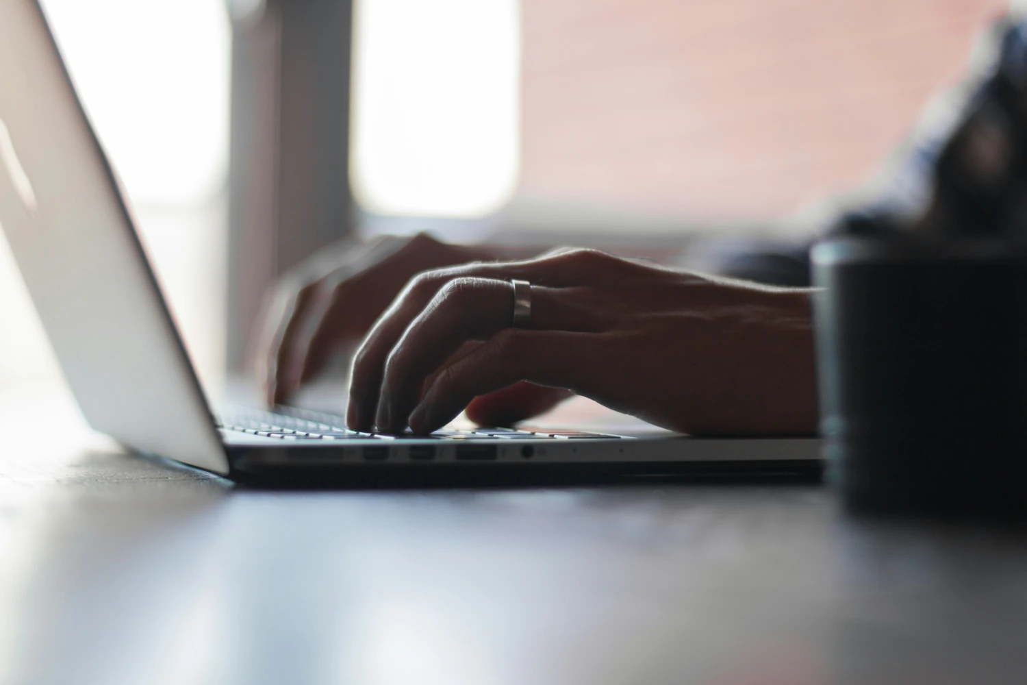 Hands typing on a laptop beside a coffee mug