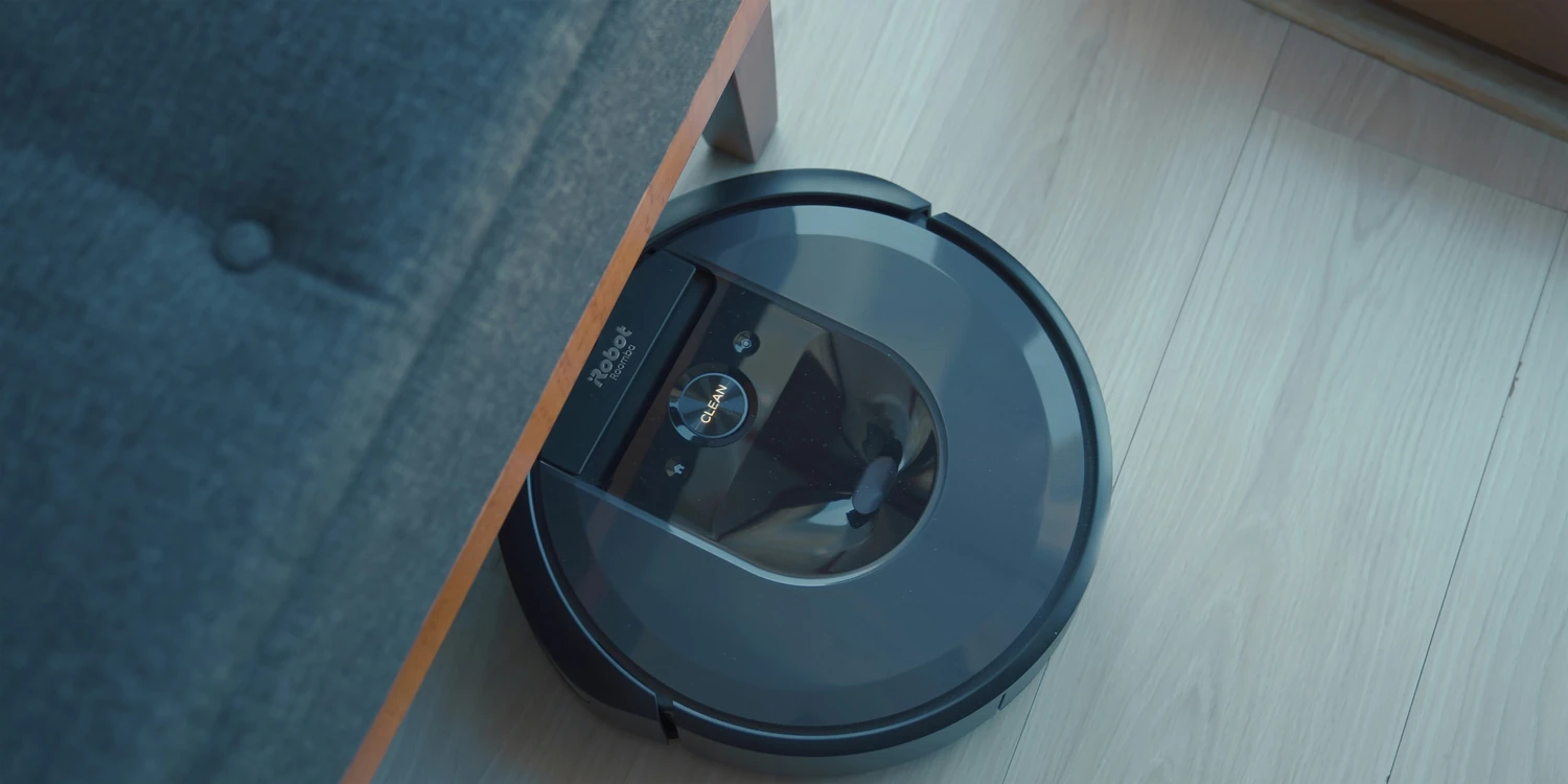 Robotic vacuum cleaning a floor beside a sofa