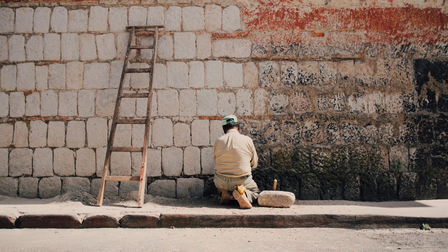 Person working beside a weathered brick wall