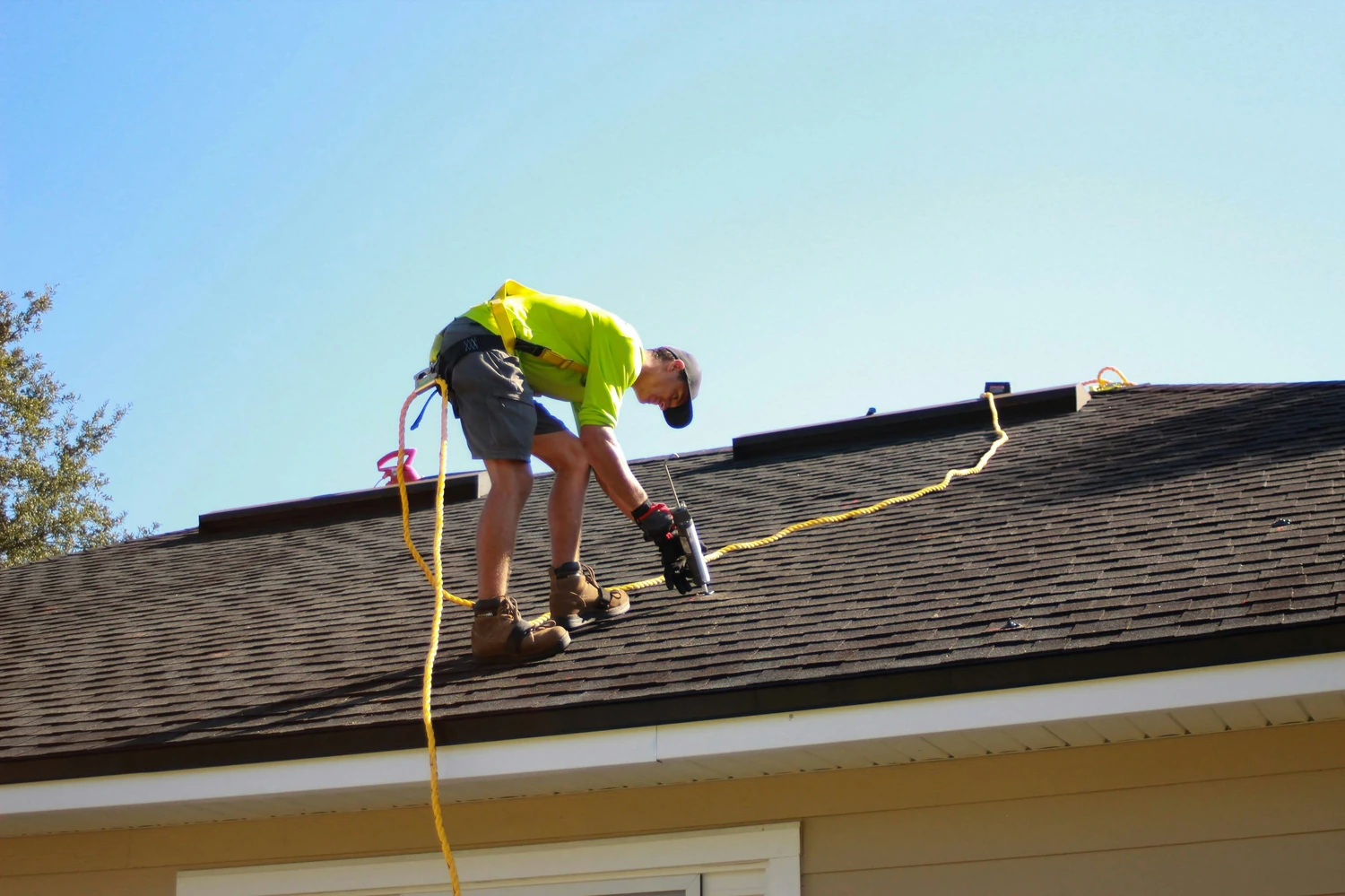 Roofer using a power tool while secured by a safety line