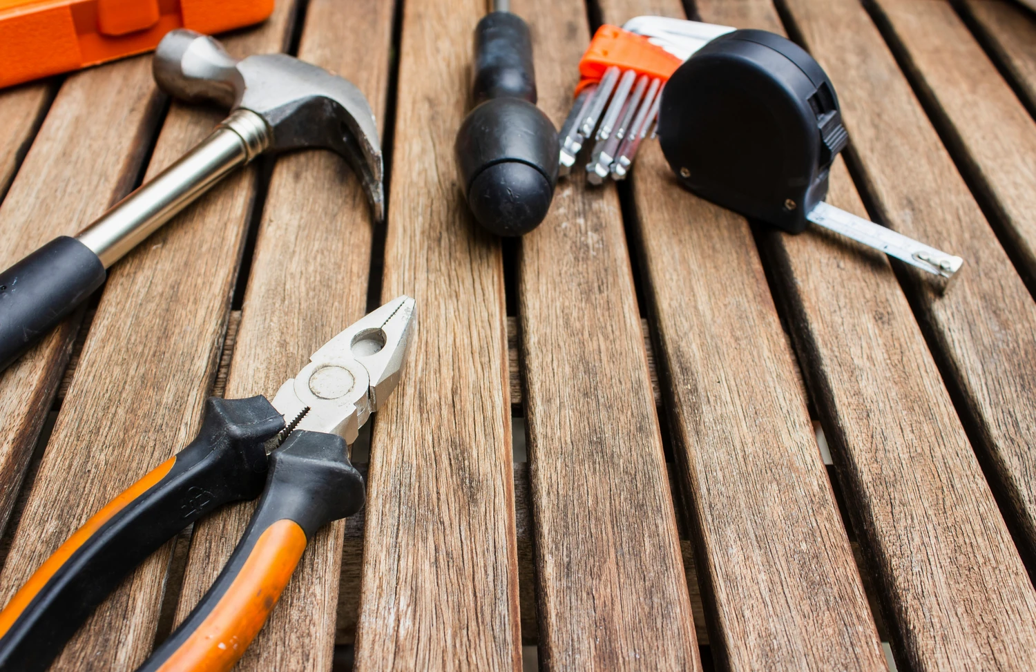 Hammer, pliers, screwdriver, tape measure, and drill on a wooden surface