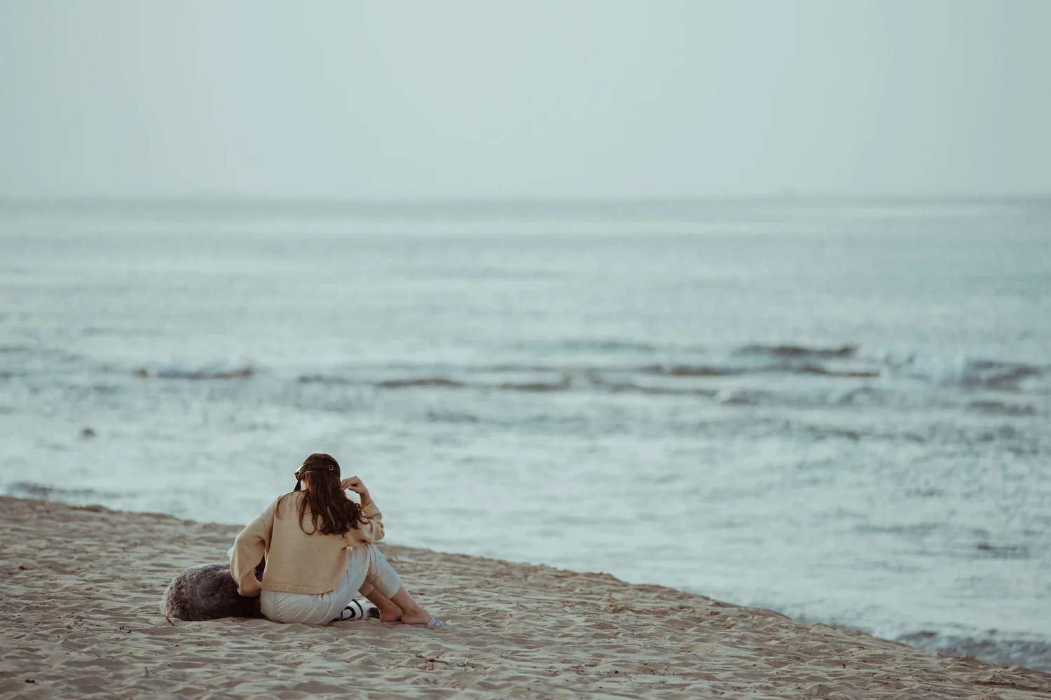 Woman sitting on a rocky shoreline facing the ocean